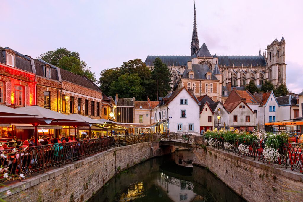 Nachtaufnahme von Amiens mit beleuchteter Kathedrale und reflektierenden Lichtern im Wasser