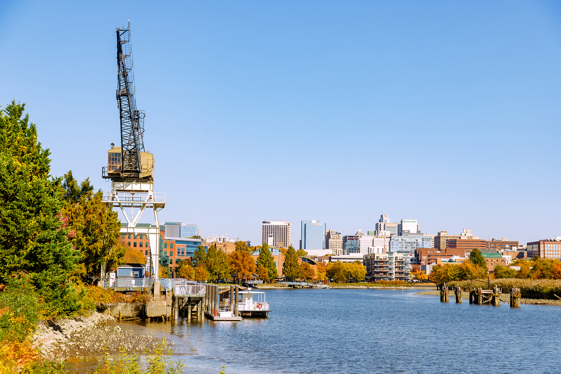 River Walk entlang des Christina River mit historischem Hafenkran und Blick auf Downtown Wilmington, umgeben von städtischer Architektur und Wasserlandschaft.